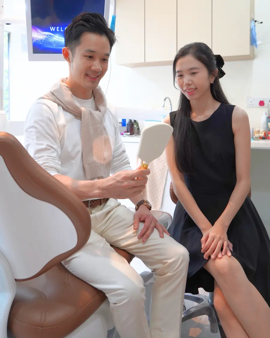 Man looking at his teeth in a hand mirror next to the dentist