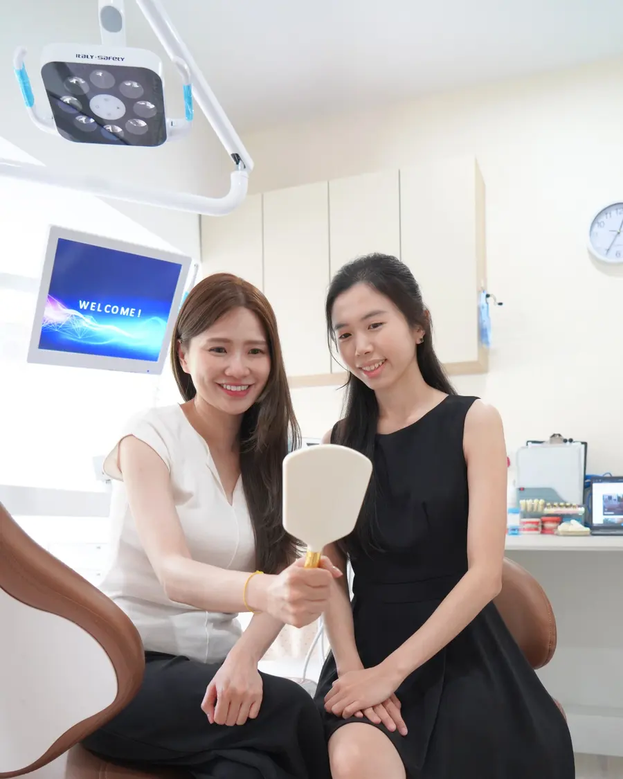 Woman checking her smile in a hand mirror beside the dentist