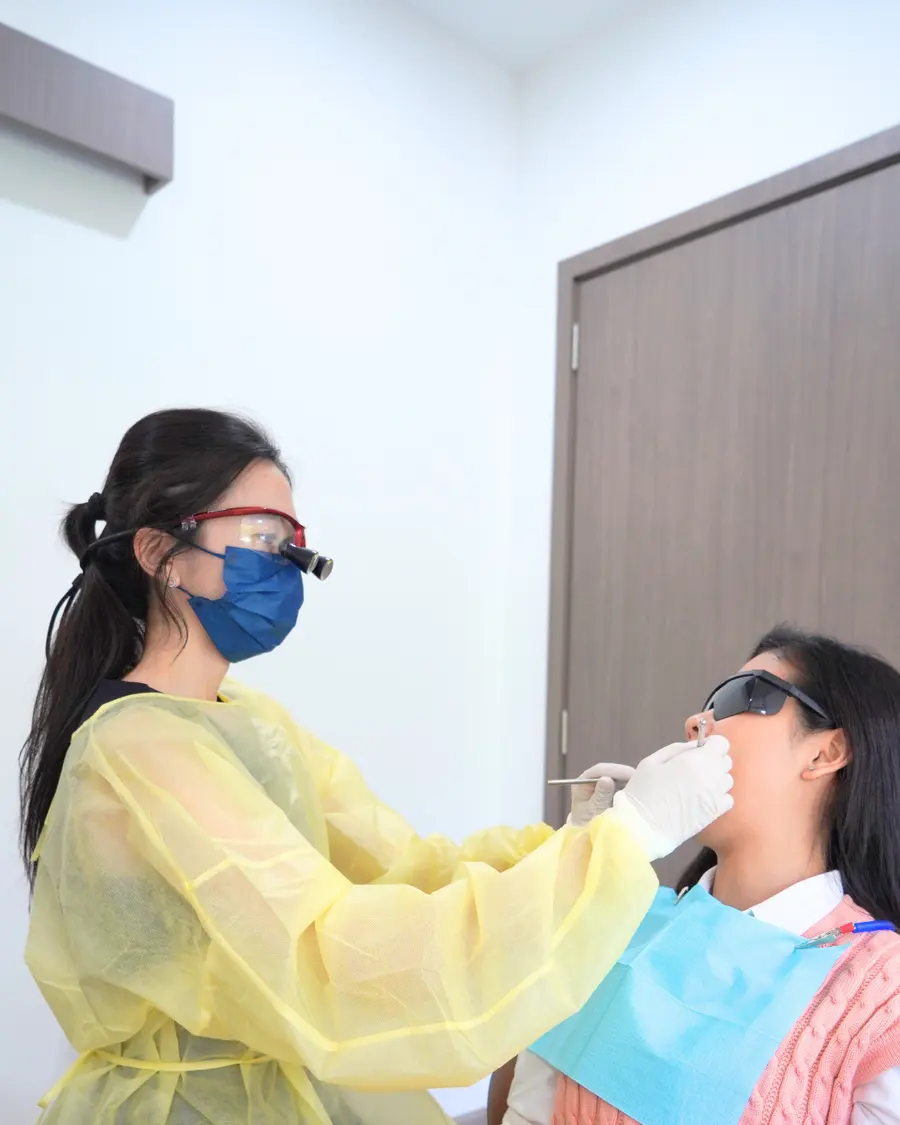 Dentist in a surgical gown and loupes examining the mouth